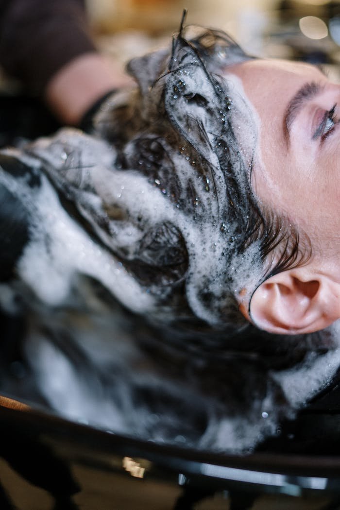 Close-up of a woman getting her hair washed at a salon, covered in shampoo foam.